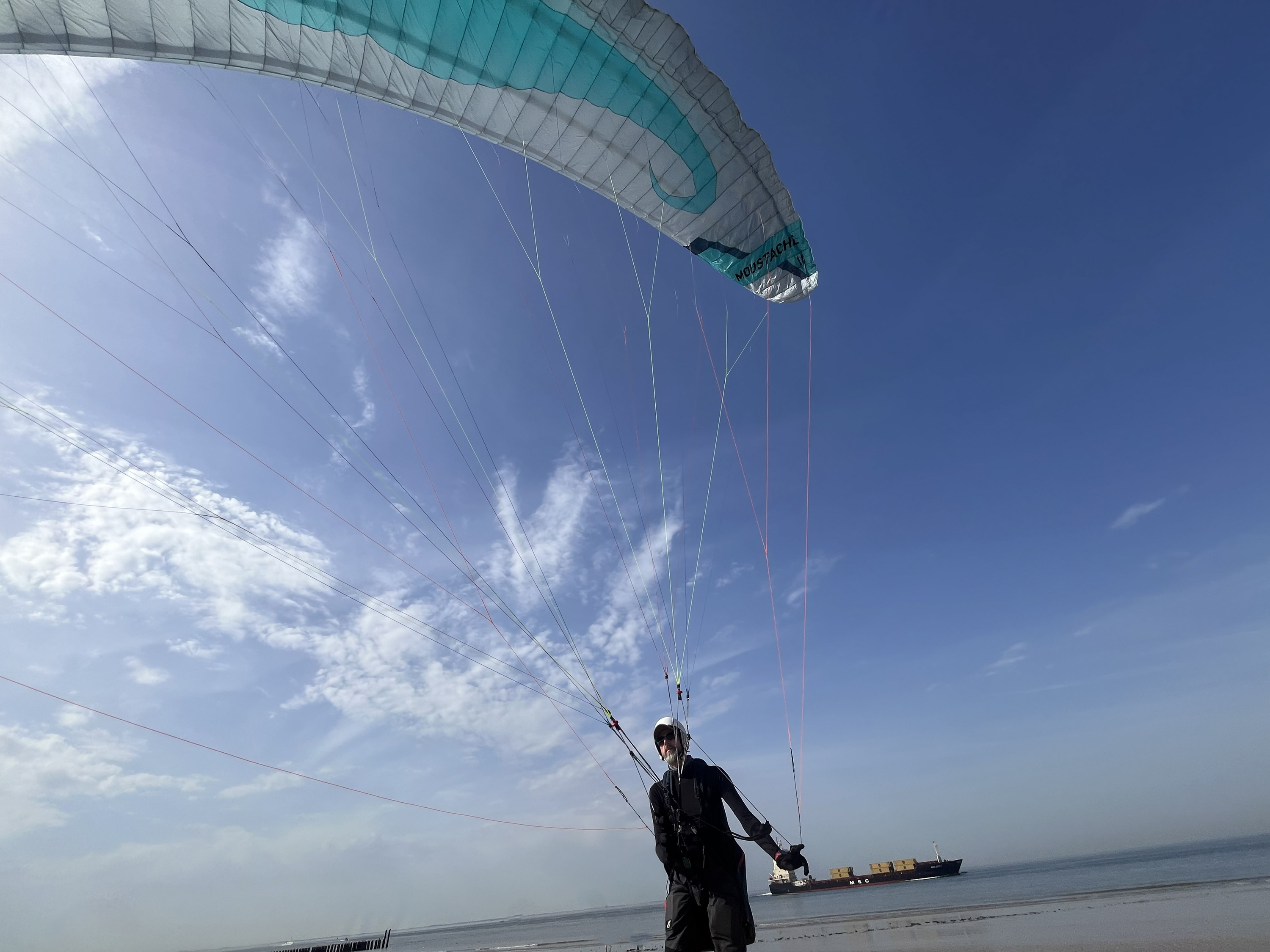 Ein Parakitepilot fliegt bei strahlendem Sonnanschein von einer Düne, der Parakite über ihm leuchtet in der Sonne.